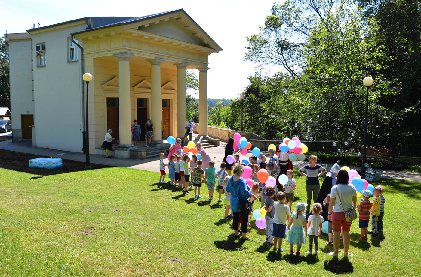 Na zdjęciu: grupa dzieci z kolorowymi balonami stoi przed budynkiem Biblioteki Miejskiej.