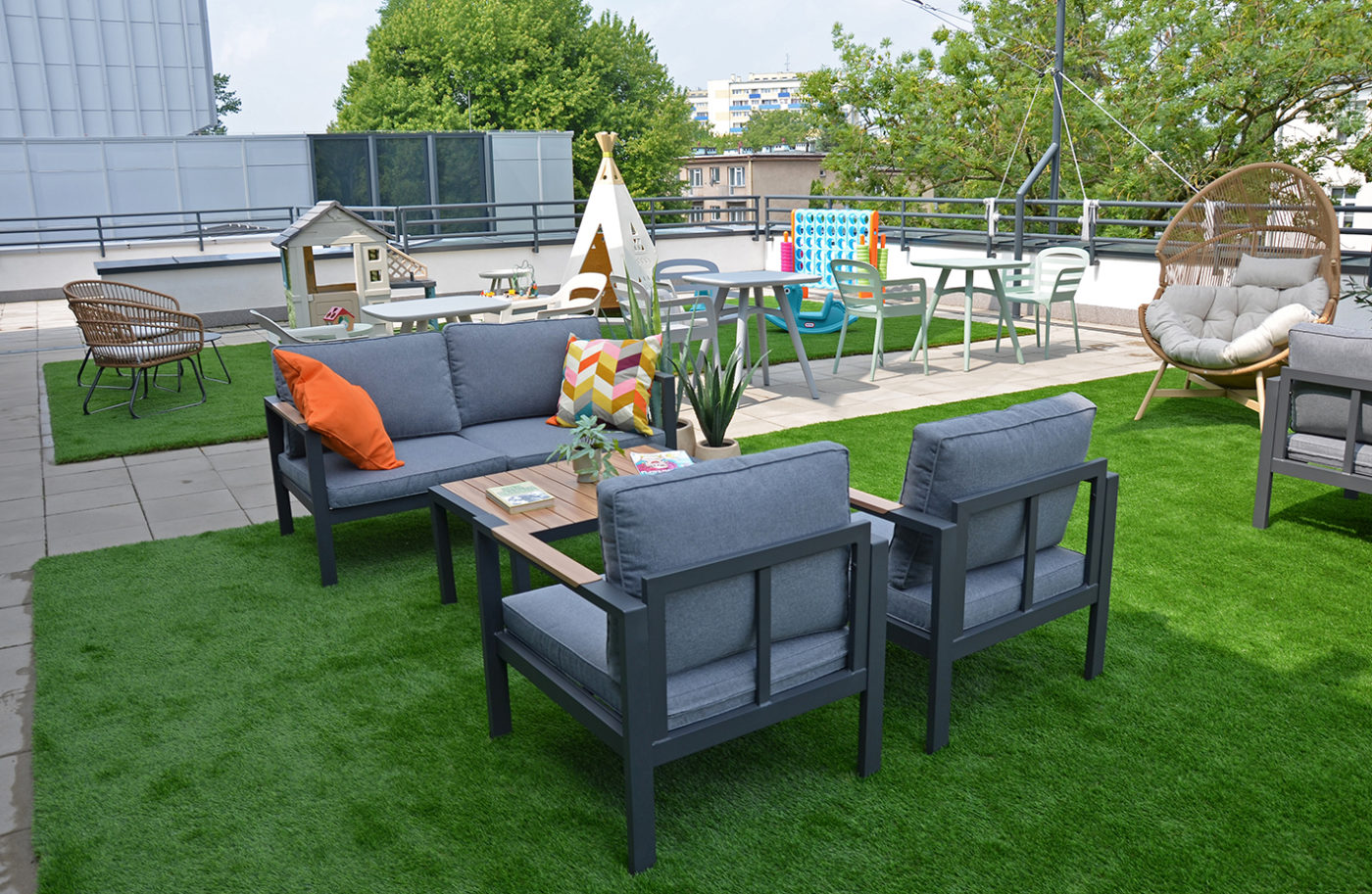 Taras Mediateki. Na zdjęciu: kanapy z poduchami, stoliki z krzesłami, na drugim planie domek dla dzieci i tipi.